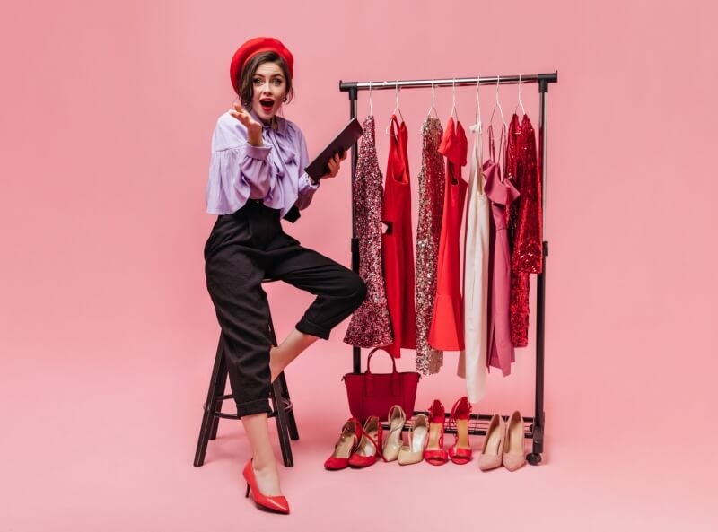 girl-purple-blouse-black-pants-is-sitting-chair-looking-into-camera-holding-folder-against-background-hangers-with-bright-dresses-min-scaled-800x593 (1)